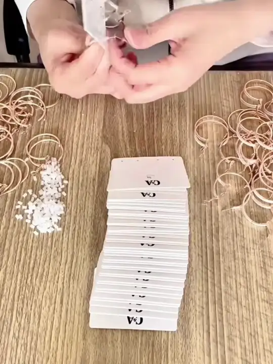 Mãos colocando pequenos acessórios em embalagens individuais.